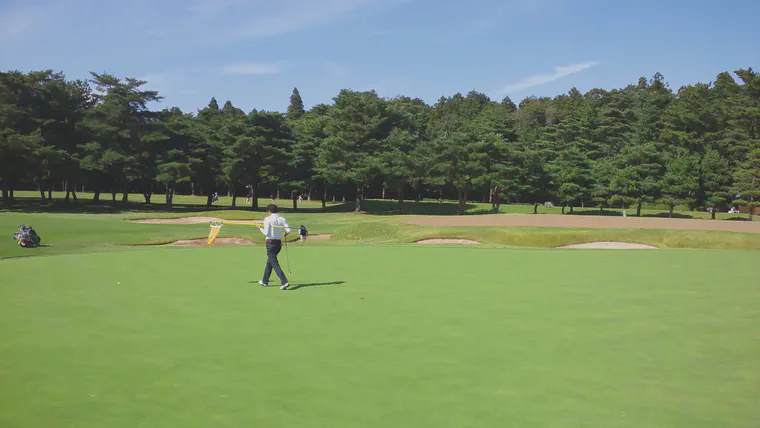 A golfer plays on one green while the other green is covered with cores.